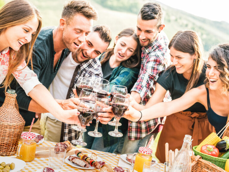 Young friends having genuine fun outdoor toasting red wine at open air bar-b-q party - Happy people eating grilled food in farmhouse vineyard winery - Youth friendship concept on warm contrast filter