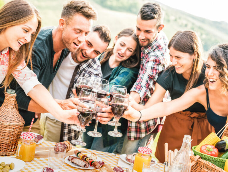 Young friends having genuine fun outdoor toasting red wine at open air bar-b-q party - Happy people eating grilled food in farmhouse vineyard winery - Youth friendship concept on warm contrast filter